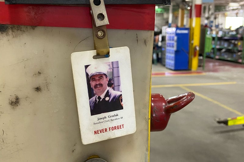 A 9/11 Memorial Stair Climb badge showing a fallen firefighter hangs at a desk workstation at Pierce Manufacturing.