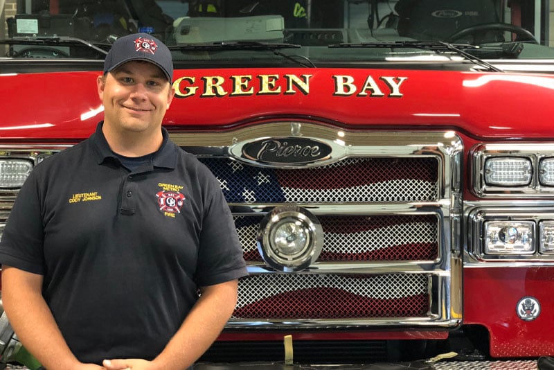 A Green Bay Metro Fire Department fire fighter stands in front of a red fire truck.