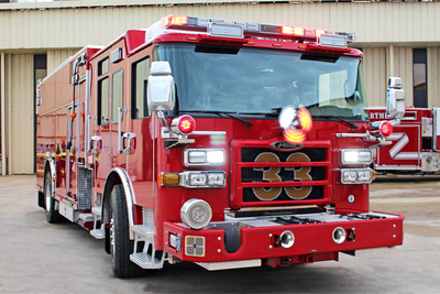 A red rescue pumper apparatus is parked outside in an industrial setting.