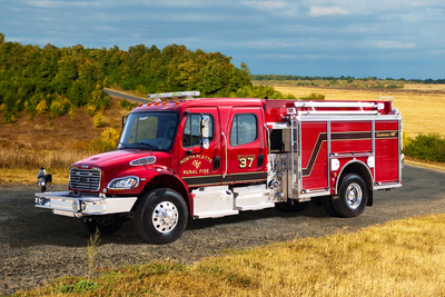A red responder pumper fire truck is parked on a grassy hill in a rural, country setting.