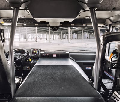 An internal view from municipal fire truck cab looking out the front window at the columns of a concrete parking structure with the driver and passenger seat visible in the foreground. 