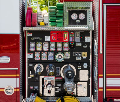 A close-up image of the pump panel of a red and white municipal fire truck. 