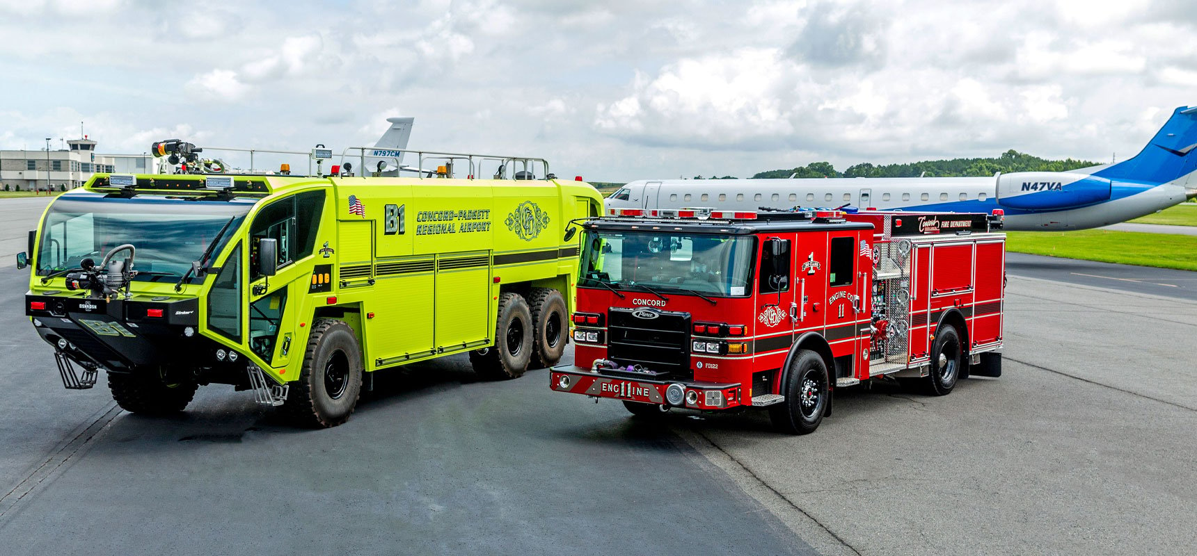A yellow airport fire truck sits next to a red municipal fire truck on an airport tarmac with a white and blue plane in the background. 