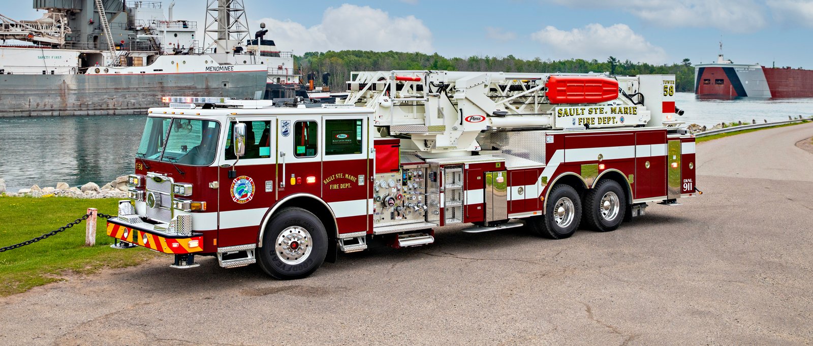 A red and white mid-mount aerial tower fire truck is parked in a large parking lot. 