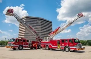 Two Overland Park Pierce aerial fire trucks parked with their ladders extended.