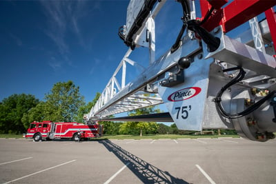 A red 75-foot aerial ladder fire truck is positioned in the background with an extended aerial device in the foreground highlighting the Pierce logo and truck name. 