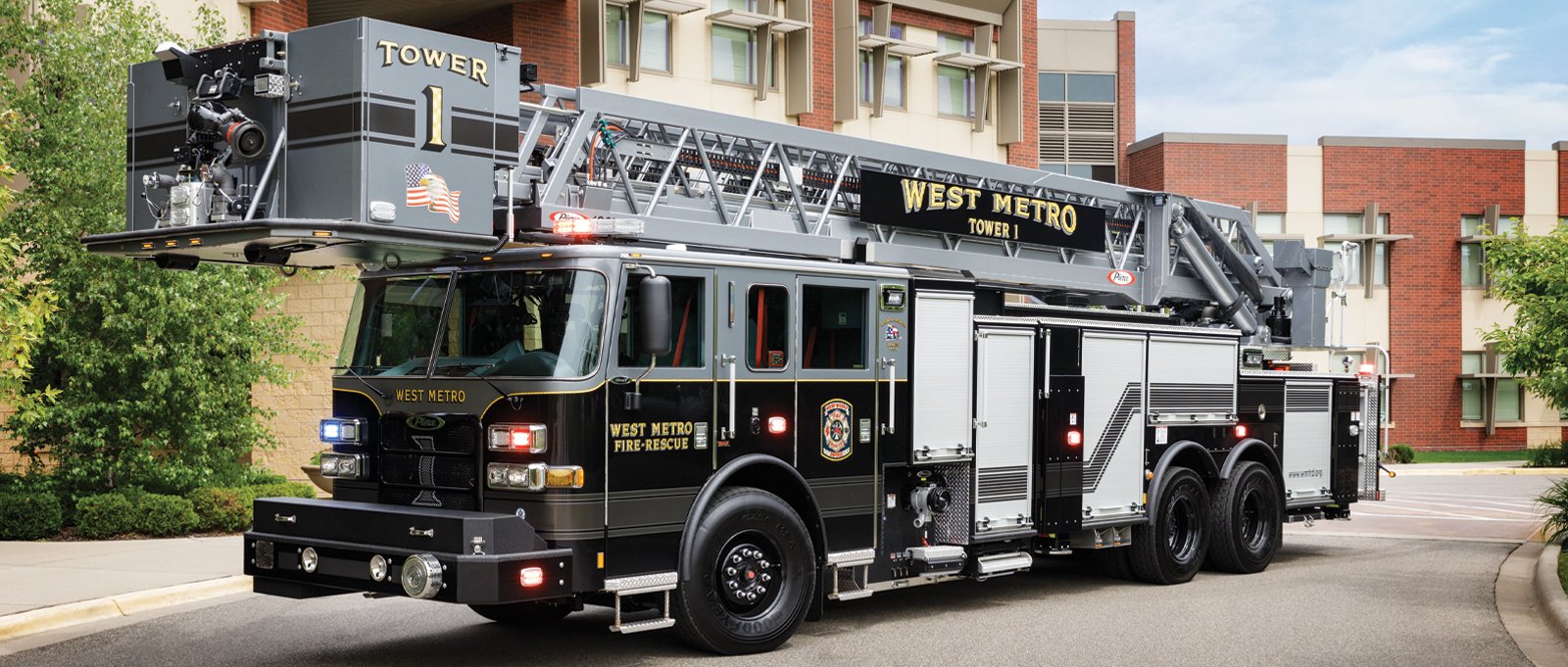 A black and grey rear-mount aerial tower is parked in front of a two-story office complex. 