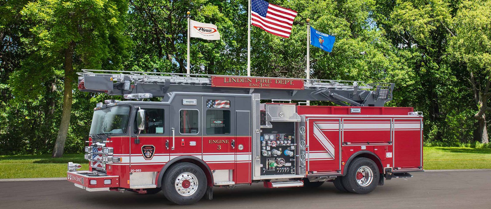 A red, white and grey water tower fire truck is pictured in front of flags and a green tree-filled background.