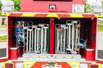 The rear end of a fire truck shows an open compartment full of internally stored ground ladders. 