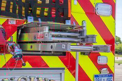 Three fire apparatus ground ladders extend out of a rear compartment on a red and yellow striped fire truck. 