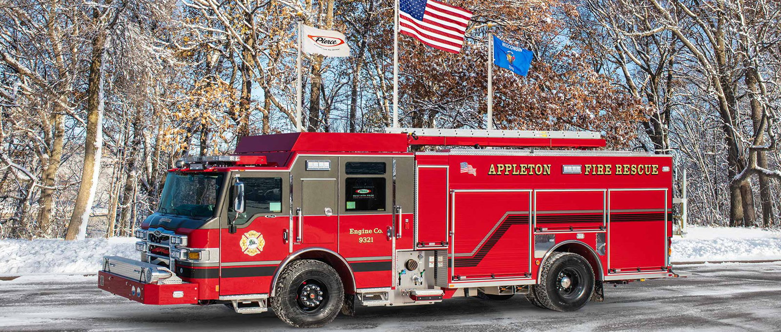 A red Appleton Fire Rescue urban fire truck is parked with flags, trees and snow in the background. 