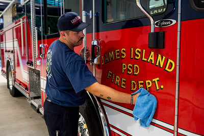 A firefighter uses a blue cloth to clean the passenger door of the cab on a red fire truck.