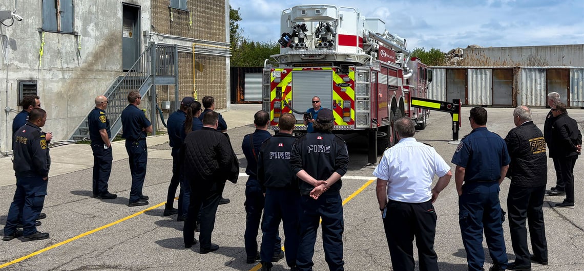 Canadian firefighters assemble around a Pierce fire apparatus as an event leader speaks during the Pierce Canadian Road Rally. 