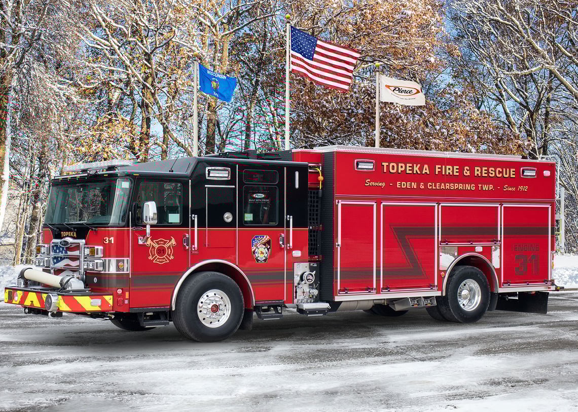 The front driver's side of a Pierce PUC heavy-duty rescue pumper in front of a three flagpoles in winter.