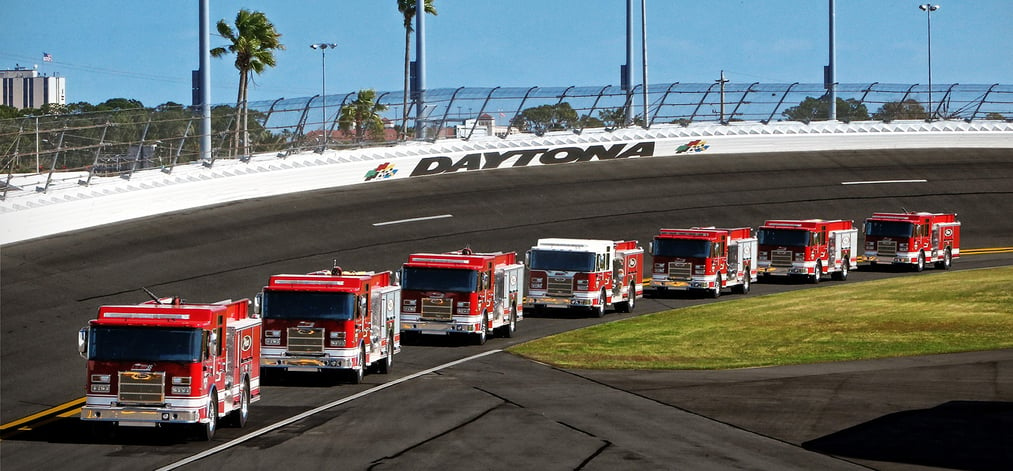 Daytona International Speedway racetrack with Pierce Manufacturing Fire Trucks in a lineup on the track.