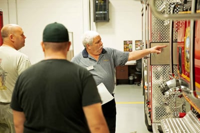 A Pierce representative completes a final inspection with two fire department representatives, pointing out design details on the side panel of the fire truck.  