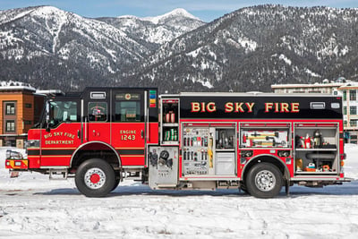 Pierce fire apparatus with all compartments open, parked in the snow with snowy mountainous surroundings.