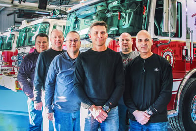 Members of the customer experience team pictures on the blue floor in front of completed fire apparatus.