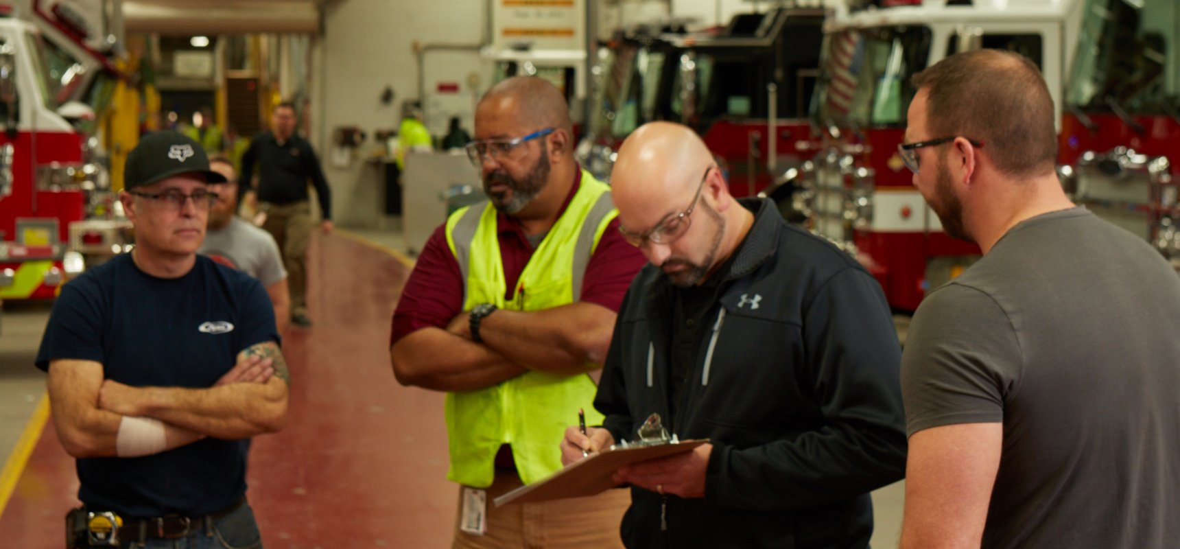 Fire department and Pierce representatives review items on a clipboard with fire trucks in the facility background.  