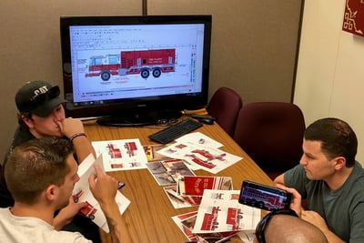 Pierce customers and team members sit around a table and computer monitor to review fire truck renderings.