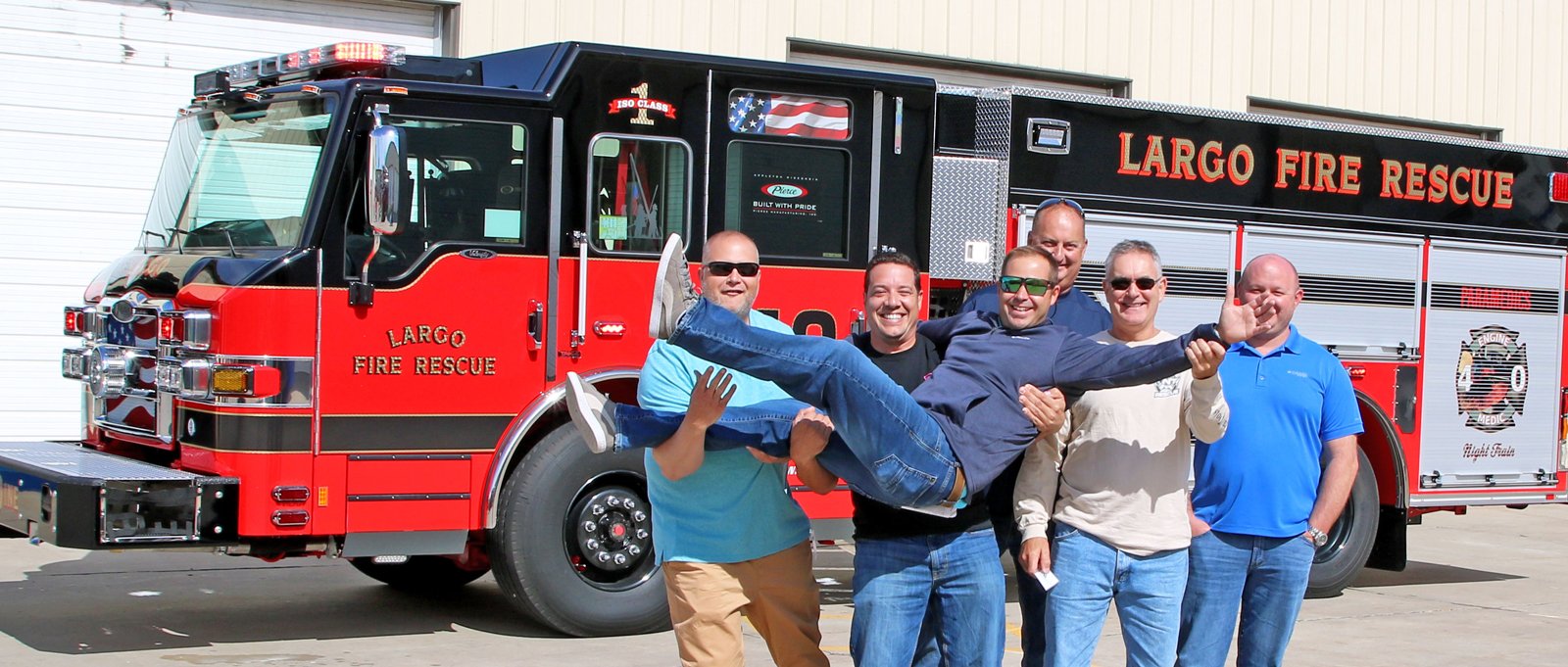 A group of fire fighters joke around with one throw in the air in front of their new fire truck at Pierce’s facility. 