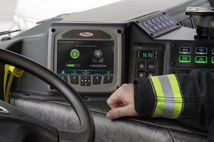 A firefighter sits in the cab next to the touch-screen used for idle reduction system command.