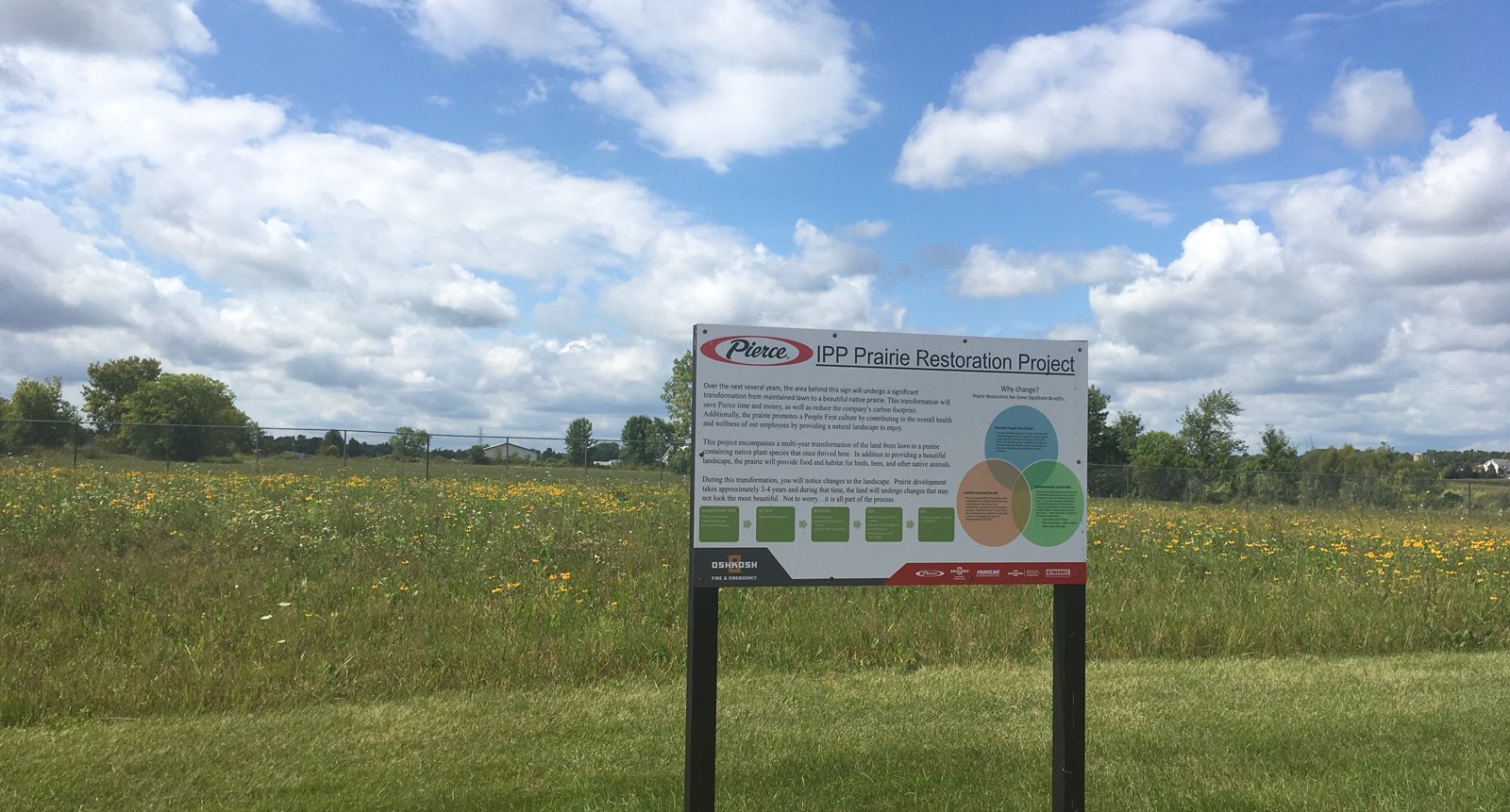Pierce Manufacturing’s IPP Prairie Restoration Project with sign in front of prairie explaining the project and Pierce’s sustainability efforts.