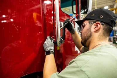 A technician works on the assembly of a red fire truck cab during the manufacturing process.