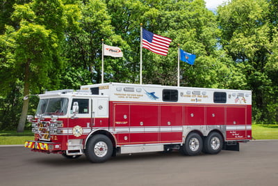 A red and white walk-in-fire truck is pictured in front of a green, tree-filled background.