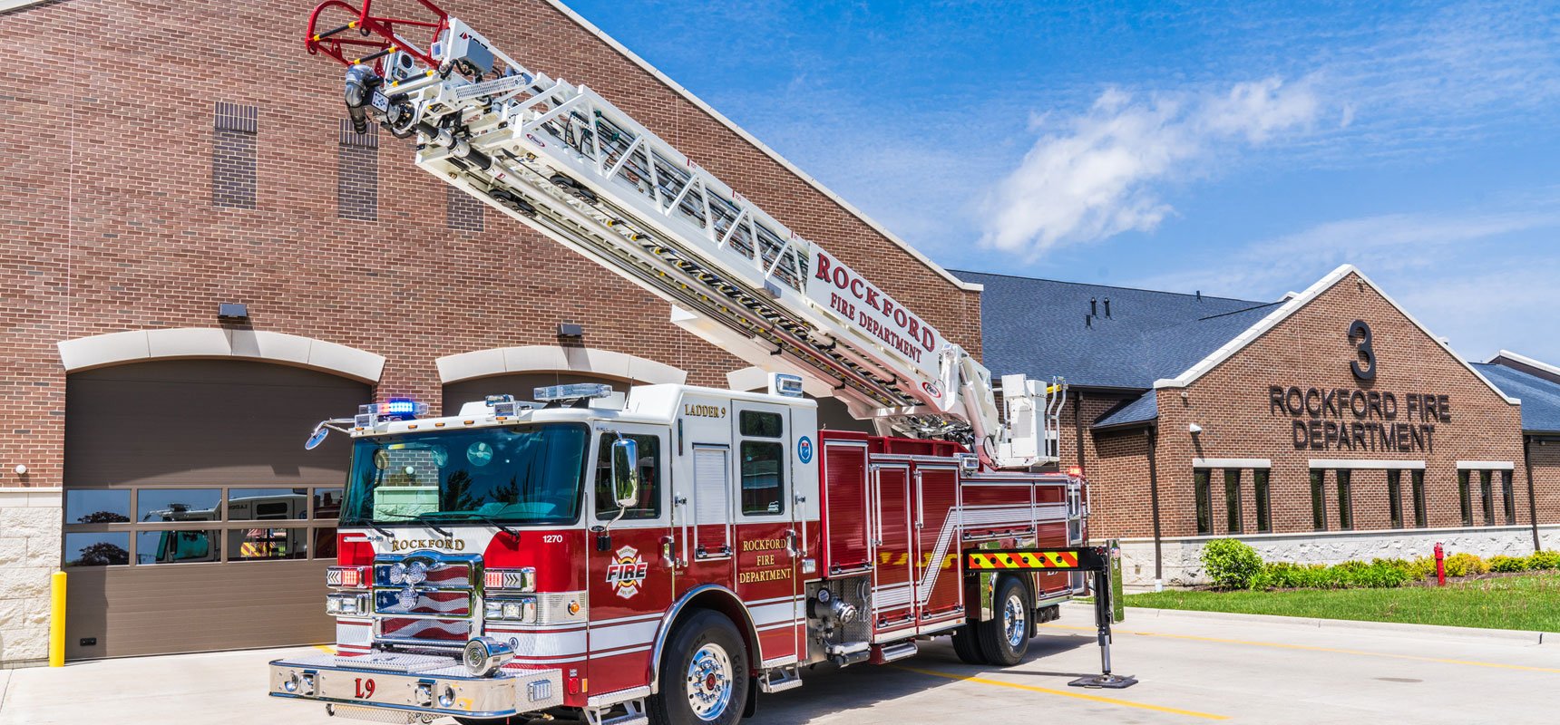 A rear-mount Ascendant aerial truck is posited with stabilizers engaged and the aerial device raised in the air.  