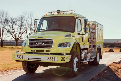 A yellow brush fire truck, or Type 3 engine, is parked to show the front of the vehicle. 