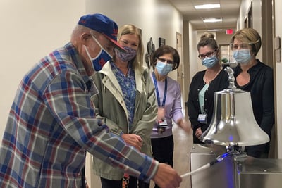 A patient rings the victory bell after his last round of cancer treatment surrounded by smiling nurses at University of Rochester WCI Greece Radiation Oncology Center.
