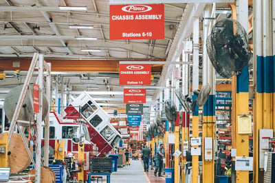 The chassis assembly area on the manufacturing floor shows many work stations and tools, as well as a fire truck cab tilted up ready for work to begin. 