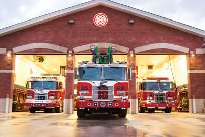 Three red and white fire trucks are pictured in the bays of a fire station.