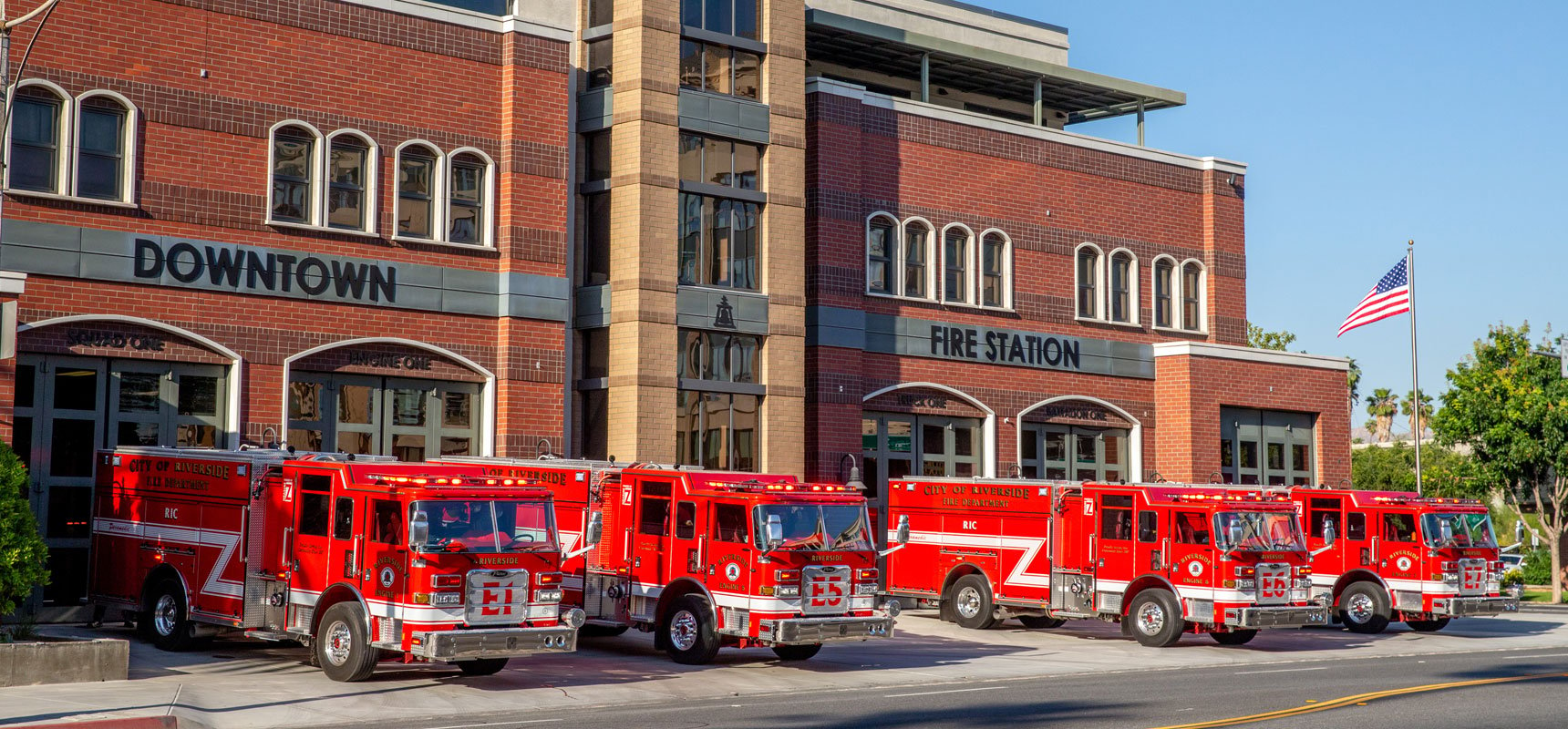 Four red fire trucks are parked outside their bays at a downtown fire station.