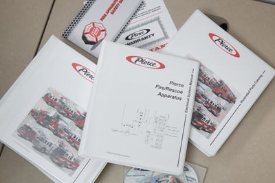 Pierce Manufacturing fire truck fleet manuals and resources are arranged on a table. 