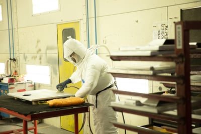 A manufacturing employee uses a sander on the surface of a fire truck part before the painting process can begin.