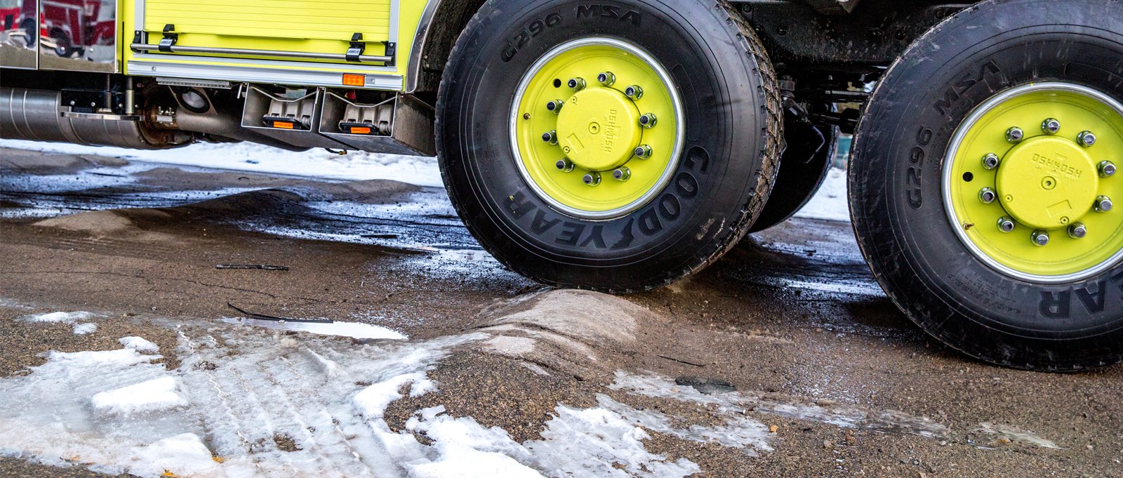 A yellow fire truck rear tire is going over a speed bump and the tire is elevated as the suspension system helps absorb the shock. 