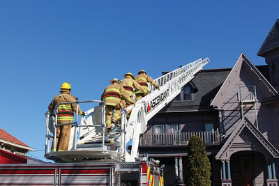 Firefighters climb an extended aerial device over a residence in a neighborhood.