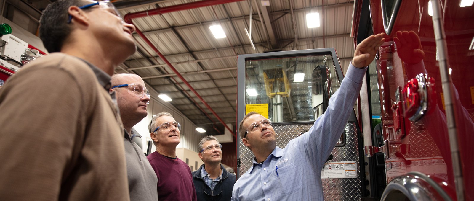 A Pierce firetruck dealer points out fire apparatus features to a group of firefighters in a Pierce Manufacturing facility. 