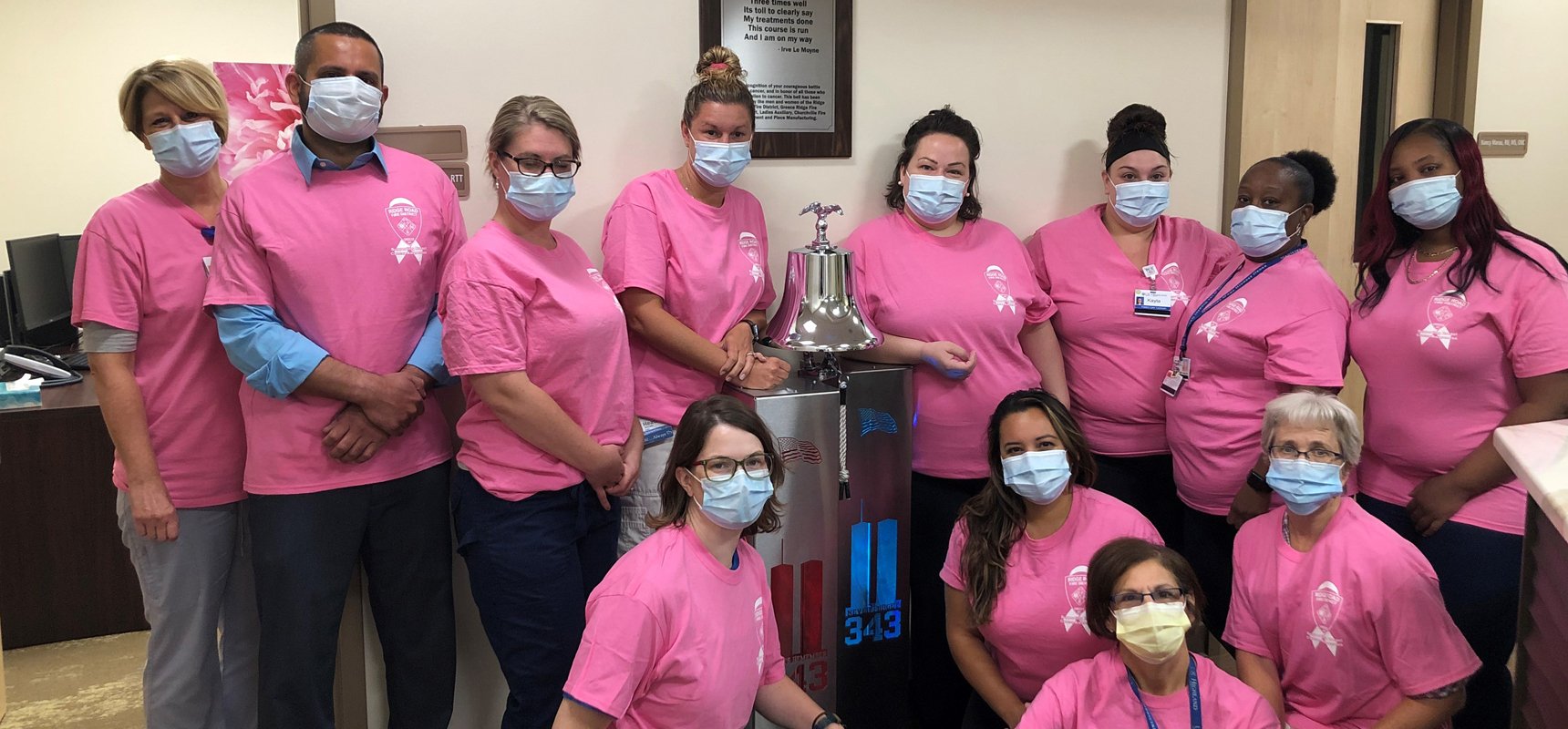 The nursing staff at University of Rochester WCI Greece Radiation Oncology Center pose in front of a victory bell, donated by the Ridge Road Fire District and Pierce Manufacturing, for cancer treatment survivors. 
