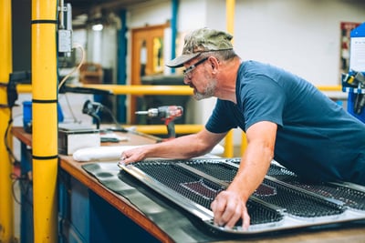 A Pierce Manufacturing team member is working on the grill of a fire truck set on a workbench.  