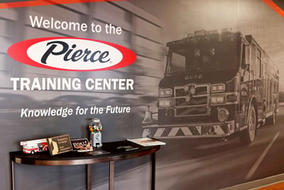 The welcome wall of the Pierce Training Center has a large black and white fire truck image and a welcome table. 