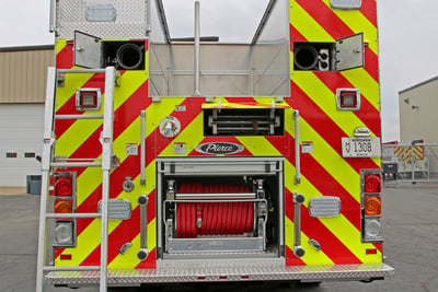 The back end of rescue pumper is pictured with yellow and orange reflective striping and a lowered ladder.