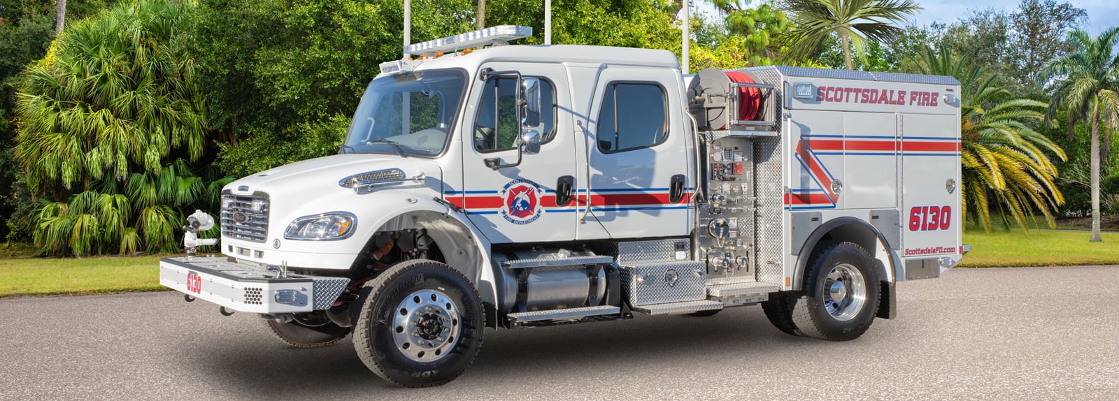 A white type 3 fire truck is parked showing the driver’s side detail with trees in the background. 