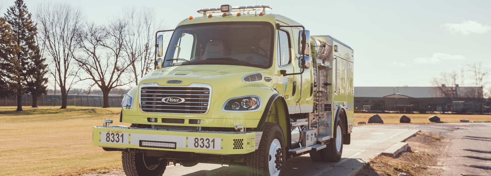 A yellow type 4 fire truck is parked facing forward showing the front end in a rural setting. 