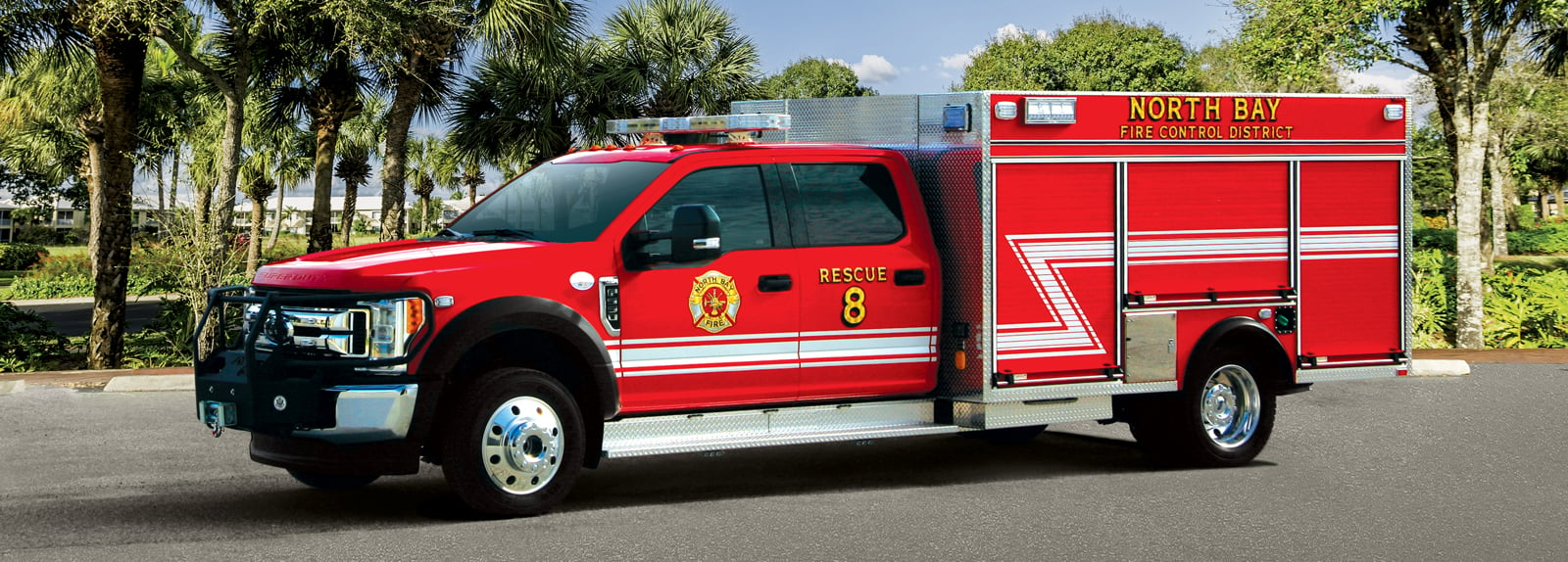 A red type-5 fire truck is parked in a lot with palm trees in the background. 