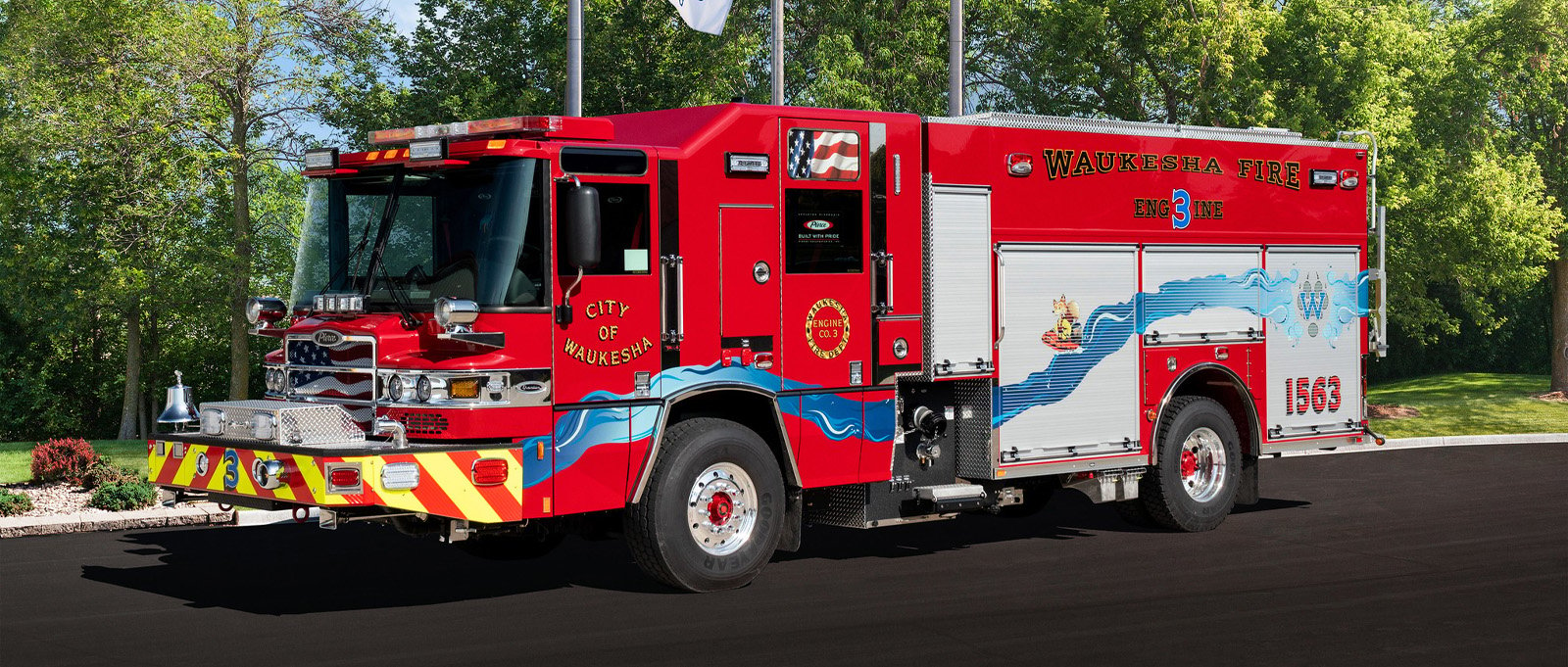 Pierce fire truck, with water graphics inspired by the Fox River from Waukesha, WI, positioned in front of the American, Wisconsin, and Pierce flags.