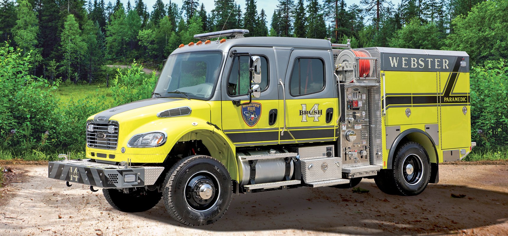 A yellow and grey wildland fire truck is parked on a dirt road with a dense evergreen forest in the background.