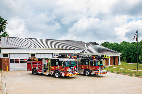 Two fire trucks parked outside fire station on partly cloudy day with American flag flying